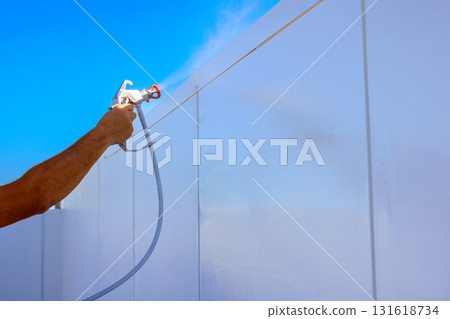 Worker is painting tall white wall with paint spray gun while workday 131618734