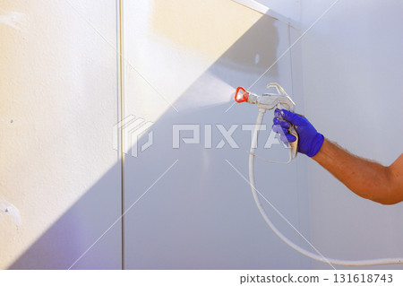 Carpenter uses spray gun to paint wall while enjoying natural sunlight in clean work environment. 131618743