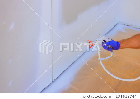 Painter uses spray gun to paint walls in room, showcasing home improvement effort during work day. 131618744