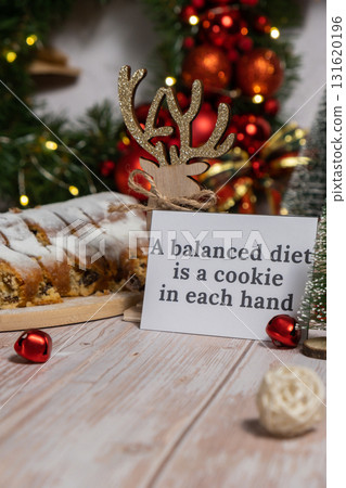 Note with saying A BALANCED DIET IS A COOKIE IN EACH HAND joke humor. Traditional German Christmas stollen cake in background of handmade festive decor. Winter holiday treats. Vegan baking recipe Note with saying A BALANCED DIET IS A COOKIE IN EACH HAND joke humor. Traditional German Christmas stollen cake in background of handmade festive decor. Winter holiday treats. Vegan baking recipe 131620196