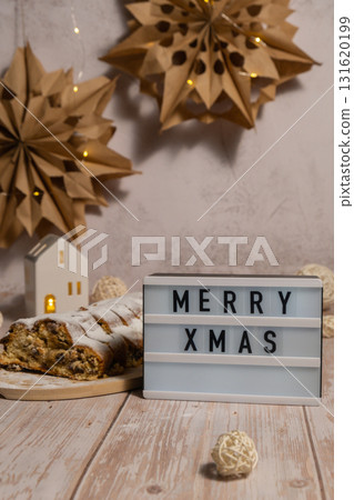 Lightbox with saying MERRY XMAS. Homemade Christmas traditional cake pie with marzipan nuts and dried fruits pastry dessert stollen. Winter holidays season atmosphere. Delicious tasty composition home 131620199