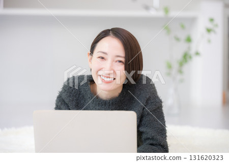 Smiling woman searching on a computer. Image of studying online at home. Lying face down in an autumn/winter knit. 131620323