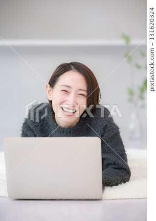 Smiling woman searching on a computer. Image of studying online at home. Lying face down in an autumn/winter knit. 131620324