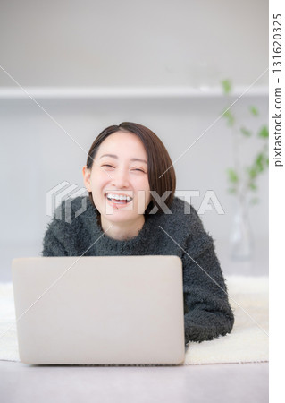 Smiling woman searching on a computer. Image of studying online at home. Lying face down in an autumn/winter knit. 131620325