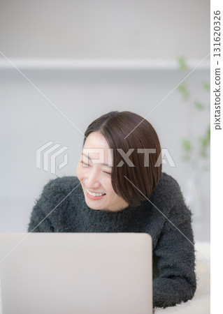 Smiling woman searching on a computer. Image of studying online at home. Lying face down in an autumn/winter knit. 131620326