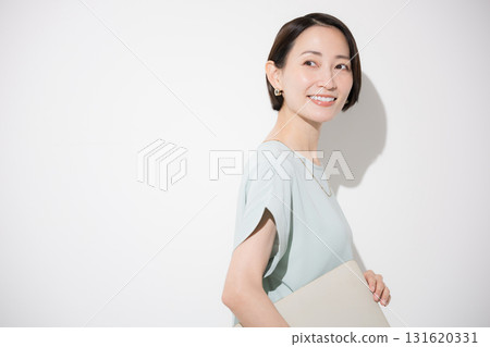 Business image of a beautiful woman standing in office casual clothes holding a laptop, looking at the camera, smiling, looking back Business image of a beautiful woman standing in office casual clothes holding a laptop, looking at the camera, smiling, looking back 131620331