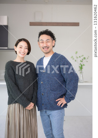 A couple in their 40s relaxing in a bright living room, looking at the camera. New home and lifestyle. Autumn/Winter. 131620462
