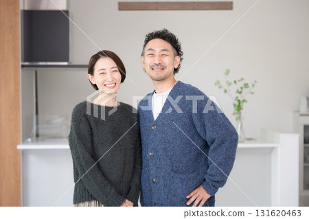 A couple in their 40s relaxing in a bright living room, looking at the camera. New home and lifestyle. Autumn/Winter. 131620463
