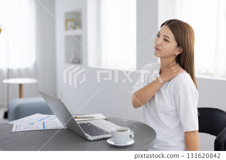 Japanese woman putting her hand on her shoulder while working on a computer 131620842