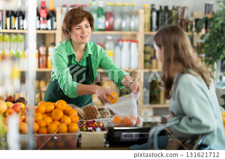 Buying ripe tangerines in store - female salesperson weighs tangerines on scales and hands them to teenage girl 131621712