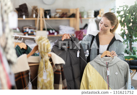 Female shopper carefully selects a fashionable jacket in clothing boutique. 131621752