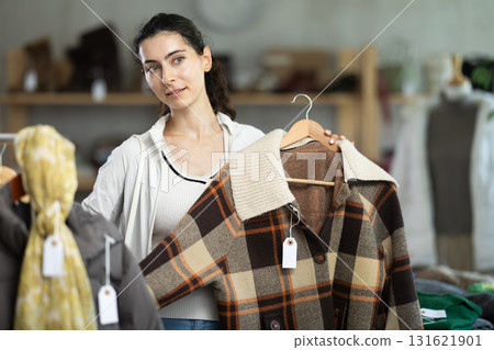 Young woman chooses plaid jacket in clothing store Young woman chooses plaid jacket in clothing store 131621901