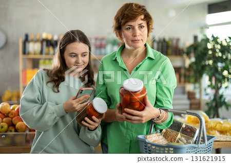Checking expiration date of pickled tomatoes - mother and daughter checking qr code on jar of pickled tomatoes 131621915
