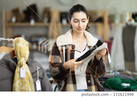 Female shopper carefully selects winter gloves in clothing store. 131621990