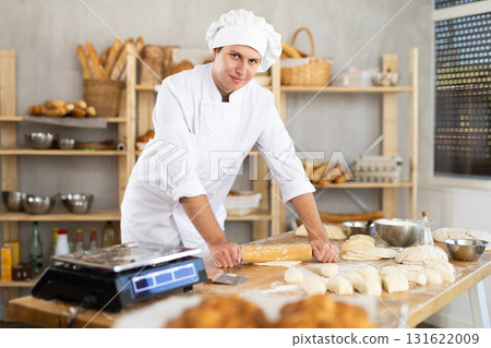 Bakery worker, young baker, rolls out raw yeast dough with rolling pin Bakery worker, young baker, rolls out raw yeast dough with rolling pin 131622009