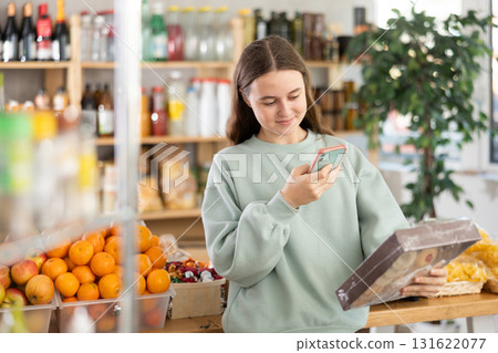 European teen girl customer at shop scans QR code on cookies package using phone camera 131622077