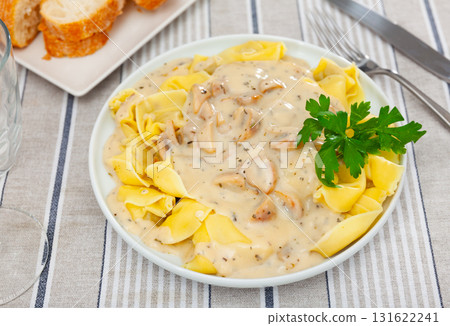Portion of fresh ravioli is served on plate, drizzled with mushroom sauce. Decorated by parsley 131622241