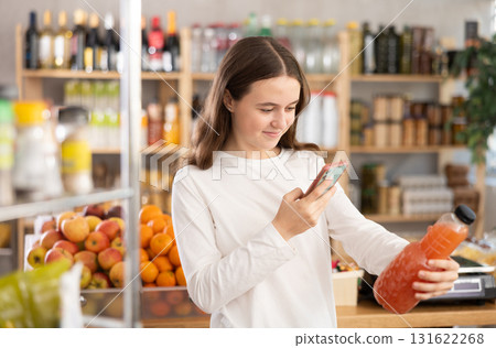 European teen girl customer at shop scans QR code on grapefruit juice bottle using phone camera European teen girl customer at shop scans QR code on grapefruit juice bottle using phone camera 131622268