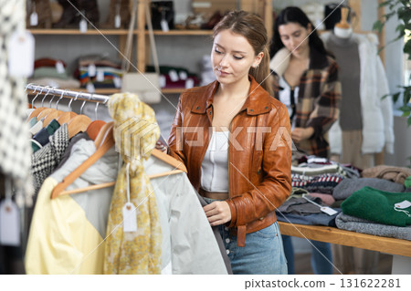 Female shopper carefully selects a fashionable jacket in clothing boutique. 131622281
