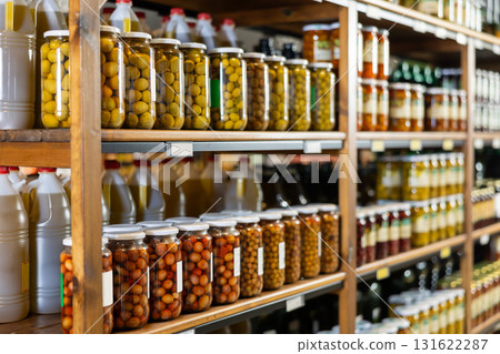 Glass jars with various pickled olives displayed on shelves in store 131622287