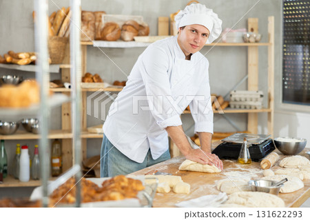 Guy baker in uniform prepares raw dough, kneads it with hands Guy baker in uniform prepares raw dough, kneads it with hands 131622293