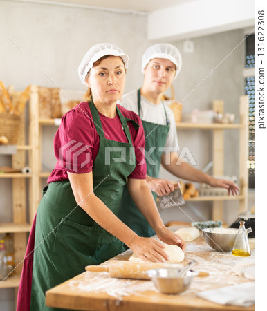 Two bakers work together to prepare dough and weigh it on scales to make croissants Two bakers work together to prepare dough and weigh it on scales to make croissants 131622308