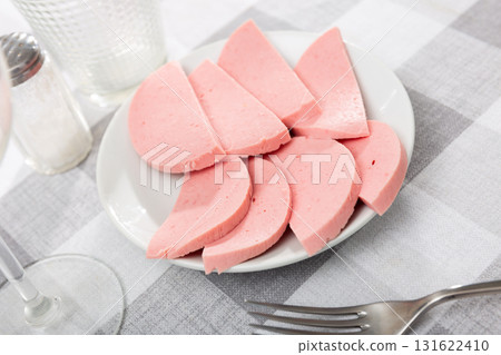 There are thick slices of boiled sausage on small round plate 131622410