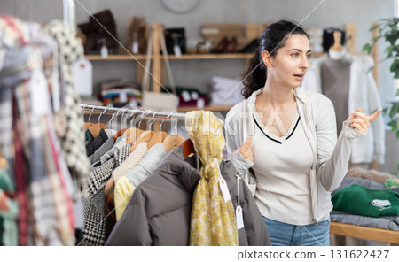 Female shopper selects clothes for autumn winter season in clothing store Female shopper selects clothes for autumn winter season in clothing store 131622427