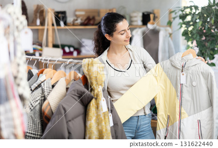 Female shopper chooses jacket in modern clothing store Female shopper chooses jacket in modern clothing store 131622440