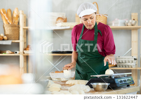 Female cook is working with dough, weighing piece of dough on scale. Female cook is working with dough, weighing piece of dough on scale. 131622447
