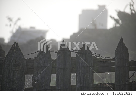 Rustic Wooden Fence With Barbed Wire And Spider Webs Against A Hazy City Background Rustic Wooden Fence With Barbed Wire And Spider Webs Against A Hazy City Background 131622625