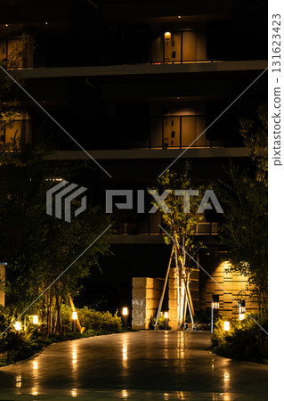 A view of the entrance to a luxury apartment building at night with warm lighting. 131623423