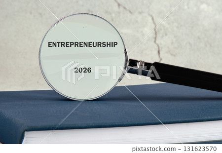 A magnifying glass rests on a stack of books, focusing on the word Entrepreneurship and the year 2026, suggesting future opportunities and business strategies 131623570