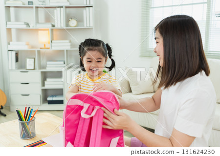 Caring mother helps cheerful daughter prepare for school with bright pink backpack in modern home environment filled with natural light and positivity Caring mother helps cheerful daughter prepare for school with bright pink backpack in modern home environment filled with natural light and positivity 131624230
