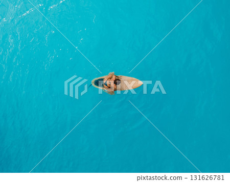 Surf girl sitting on surfboard in blue ocean. Aerial view 131626781