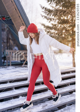Young woman walking down snowy stairs in a winter outfit while enjoying a sunny day at a cozy retreat Young woman walking down snowy stairs in a winter outfit while enjoying a sunny day at a cozy retreat 131628593