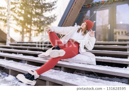 Young woman enjoying winter outdoors with stylish outfit on wooden stairs in a snowy landscape during sunrise 131628595