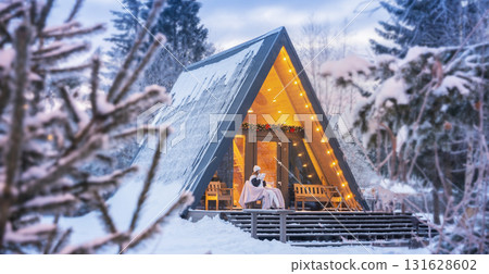 A trip to the winter forest and a morning tea party in a magical triangular house in a coniferous forest. A woman drinks coffee early on Christmas morning panorama 131628602