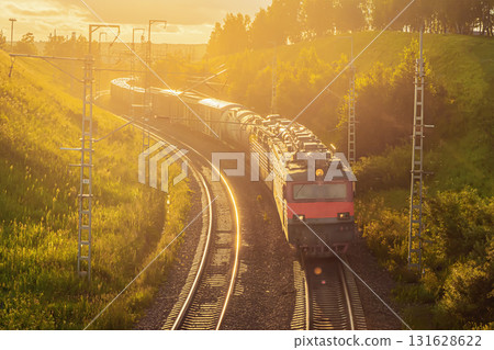 A freight train, comprised of a powerful locomotive and various freight wagons including oil tanks, gracefully navigates a winding railway track. 131628622