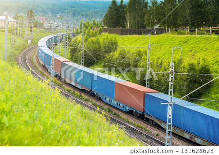 Railway container transportation . A railway train with containers drives winding through a green hilly rural area 131628623