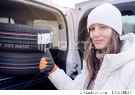 Happy woman loads new tires into her car trunk for seasonal tire change in winter. purchase and sale of new tires for the season. 131628625