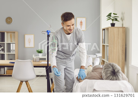 Young friendly nurse help senior patient in receiving IV drip infusion therapy in clinic 131629701