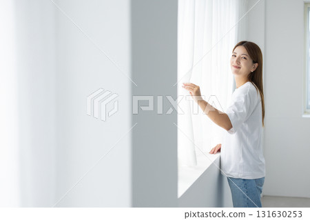 站在窗邊沐浴自然光的微笑年輕女子 131630253