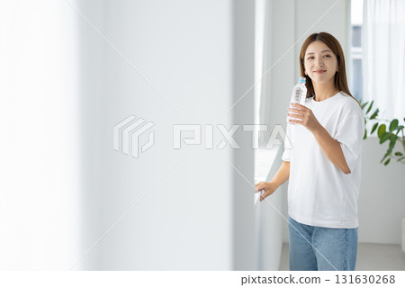 A Japanese woman holding a bottle of water while soaking up the natural light by the window A Japanese woman holding a bottle of water while soaking up the natural light by the window 131630268