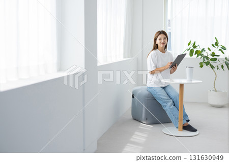 一位年輕女子在明亮的房間裡操作平板電腦 131630949