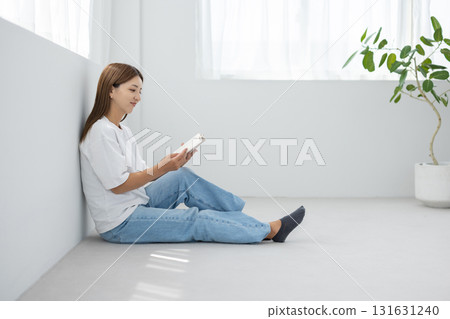 一位年輕女子坐在明亮的房間的地板上，享受閱讀 131631240