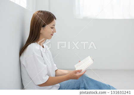 一位年輕女子坐在明亮的房間的地板上，享受閱讀 131631241