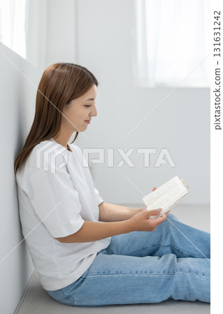 一位年輕女子坐在明亮的房間的地板上，享受閱讀 131631242