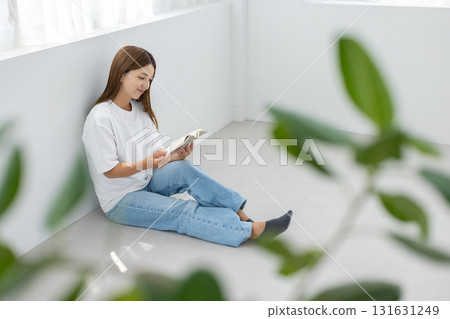 A young woman sitting on the floor in a bright room and enjoying reading A young woman sitting on the floor in a bright room and enjoying reading 131631249