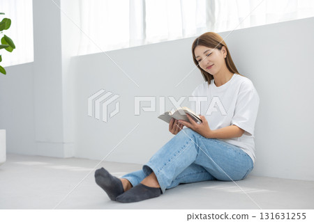 一位年輕女子坐在明亮的房間的地板上，享受閱讀 131631255
